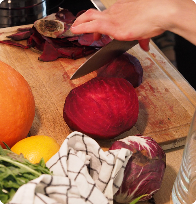 Eine halbierte Roote Beete auf einem Holzbrett mit dem Messer und einer Hand darüber
