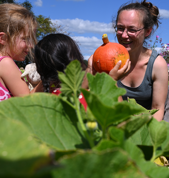 zwei Kinder und eine erwachsene Person gut gelaunt auf einem Feld mit einem Kürbis in der Hand